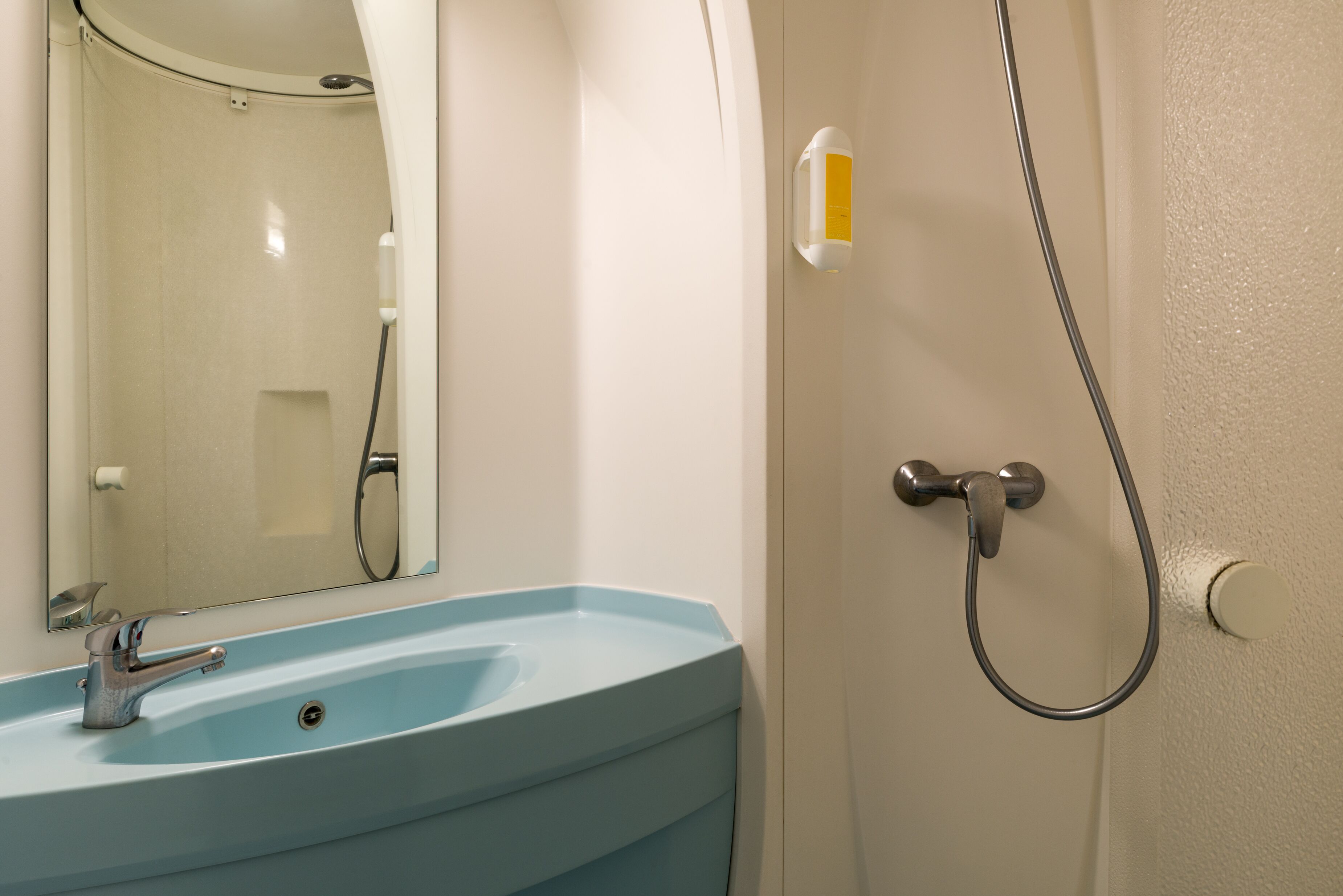 A bathroom with a blue sink, a mirror, a shower, and a soap dispenser.