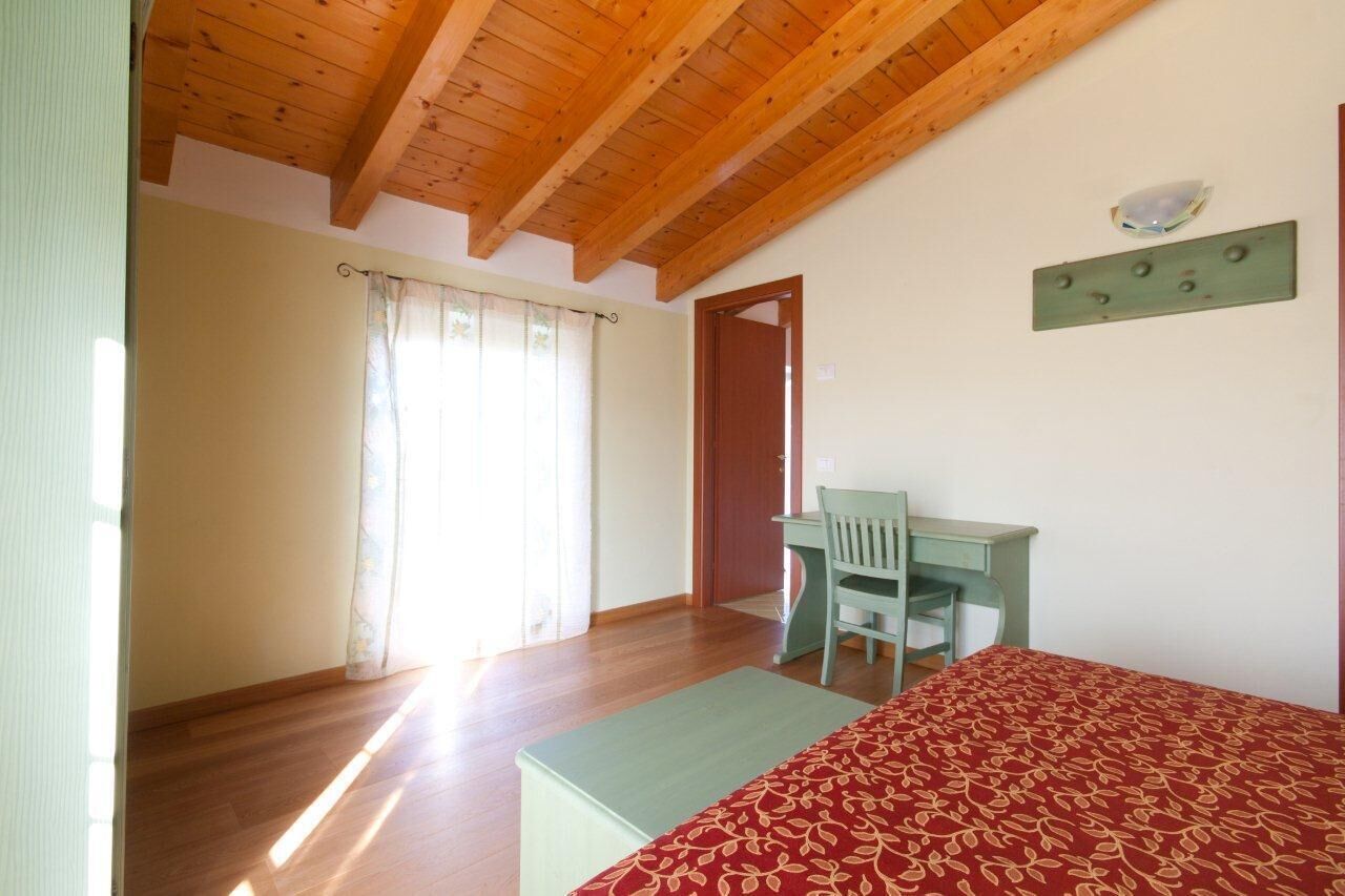 Un dormitorio con techo de madera, una cama con colcha estampada, un escritorio con silla y una ventana con cortinas.