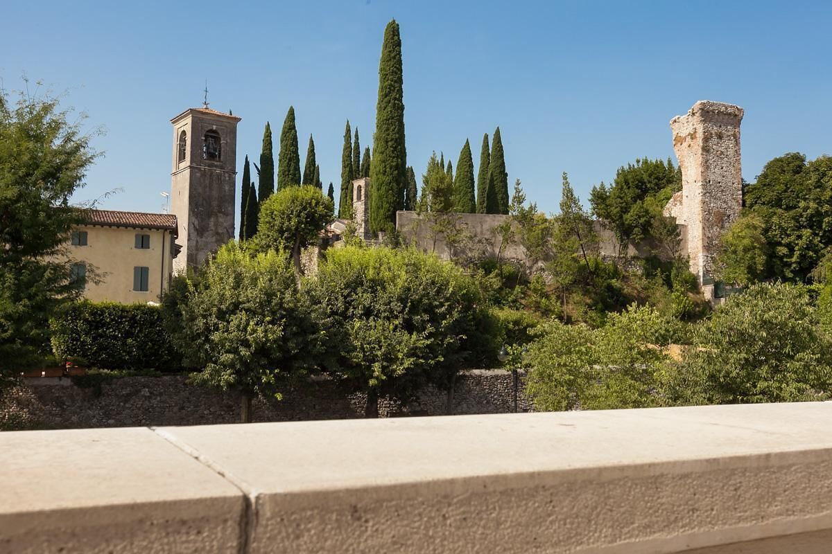 A historic stone tower, a church with a bell tower, and a tall cypress tree.