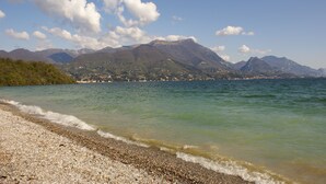 A pebbled beach with a view of mountains and a clear sky. - Barchi Resort - Apartments & Suites (San Felice del Benaco)