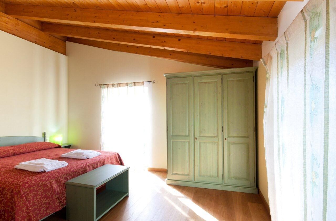Una camera da letto con un letto, un armadio verde, una panca e una finestra con tende.