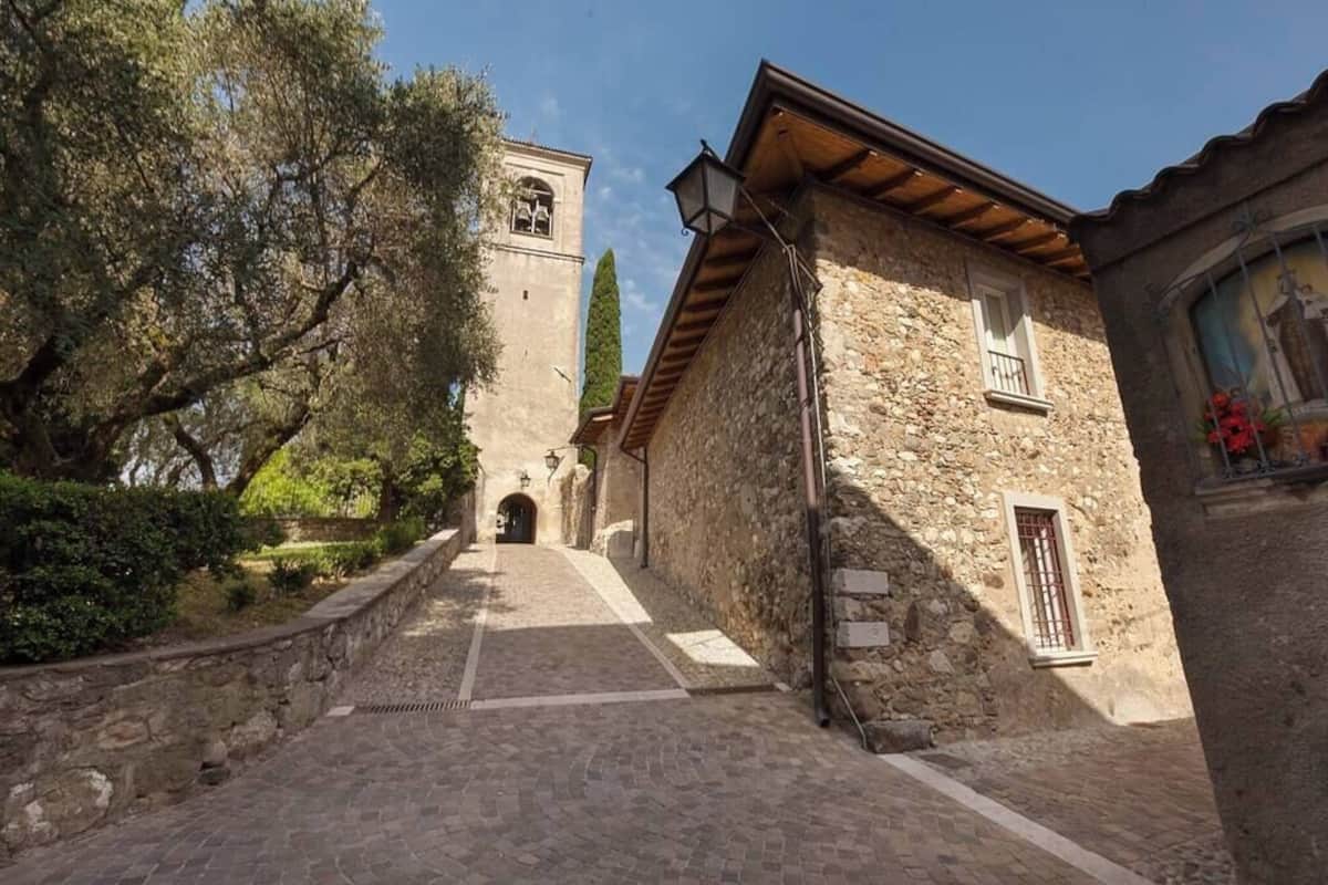 A stone building with a bell tower, a narrow cobblestone path, and a small window with a flower box.