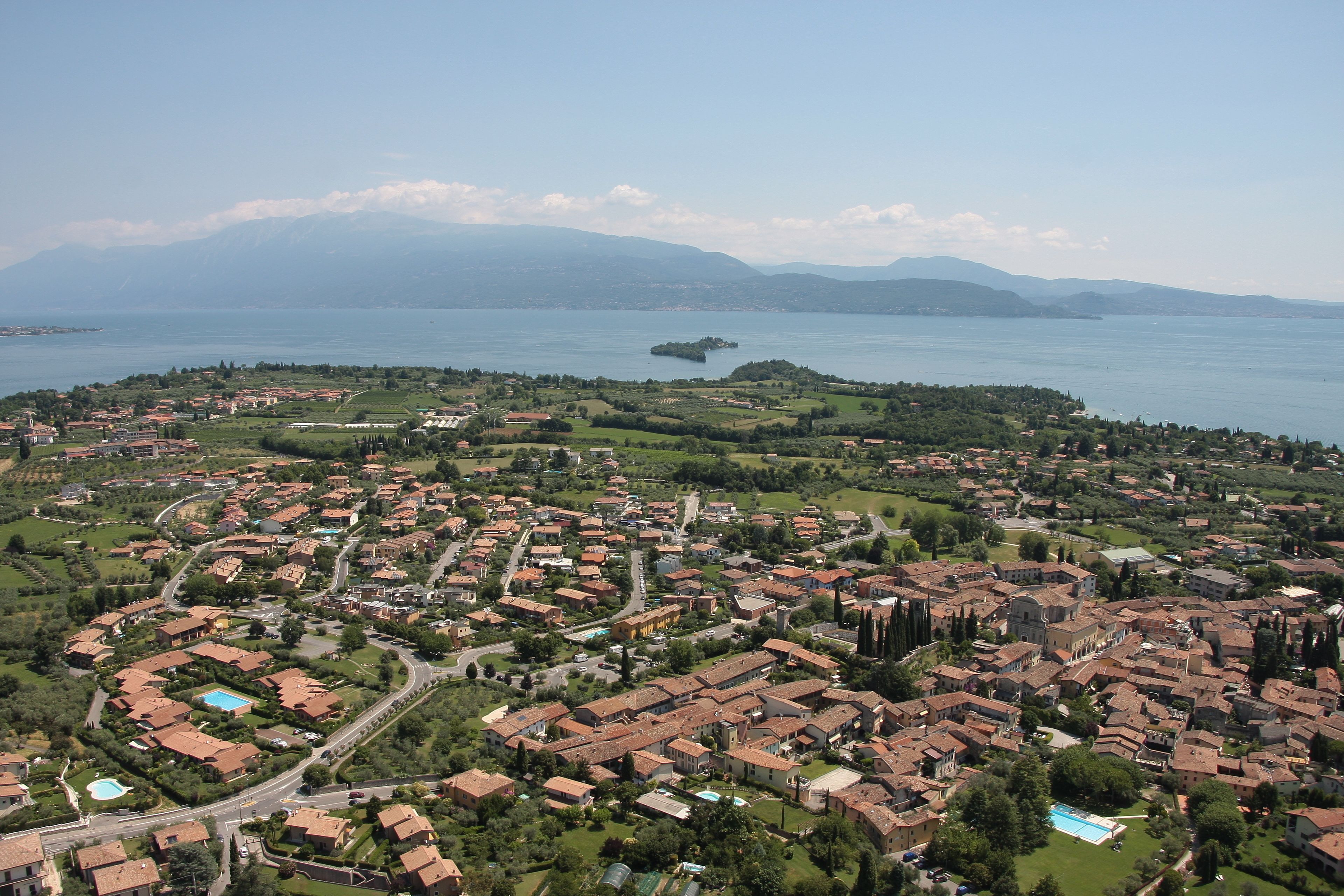 Una vista aerea di una cittadina costiera con edifici residenziali, strade e una vasta distesa d'acqua.