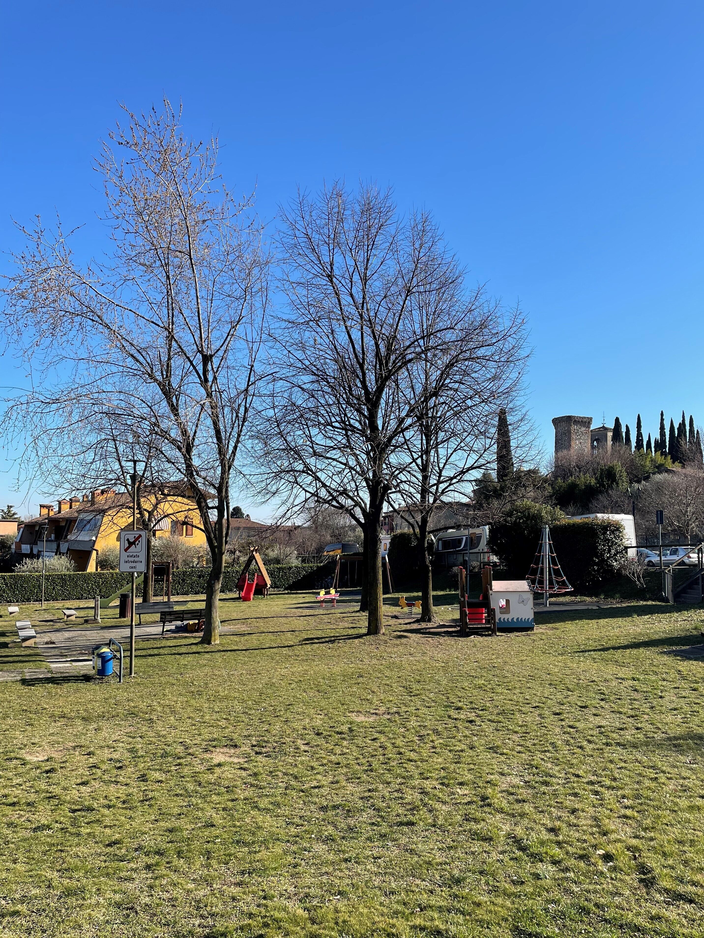 A park with playground equipment, a sign prohibiting dogs, and a castle-like structure in the background.