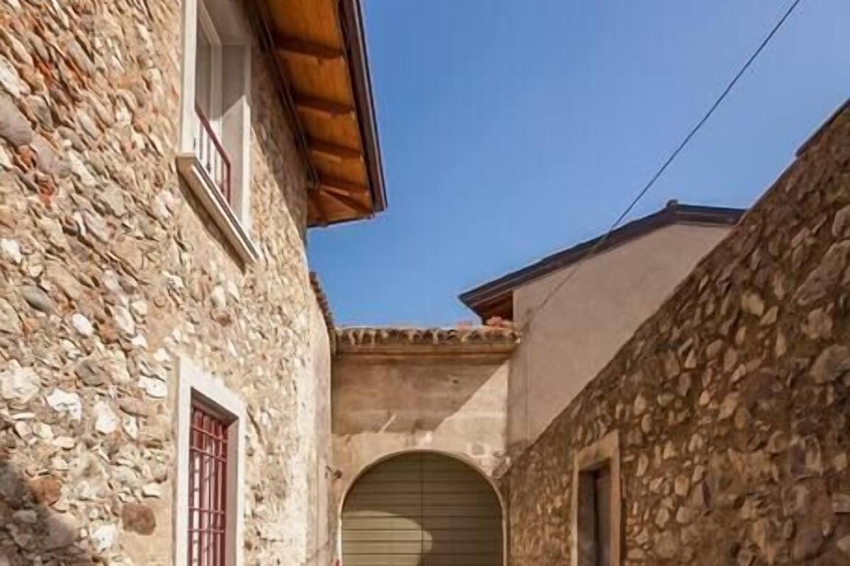 A narrow stone alleyway with a cobblestone path, a wooden door, and a window with a metal grille.