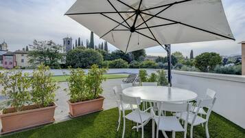 A rooftop terrace with a round table and chairs, surrounded by terracotta planters and a large umbrella.