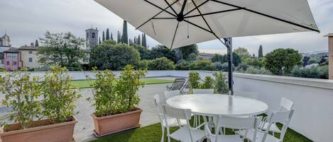 Une terrasse sur le toit, avec une table ronde et des chaises, entourée de jardinières en terre cuite et d’un grand parasol.