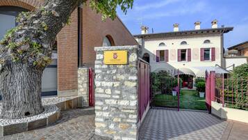 A stone pillar with a plaque, a brick building, and a gated entrance with a small garden.