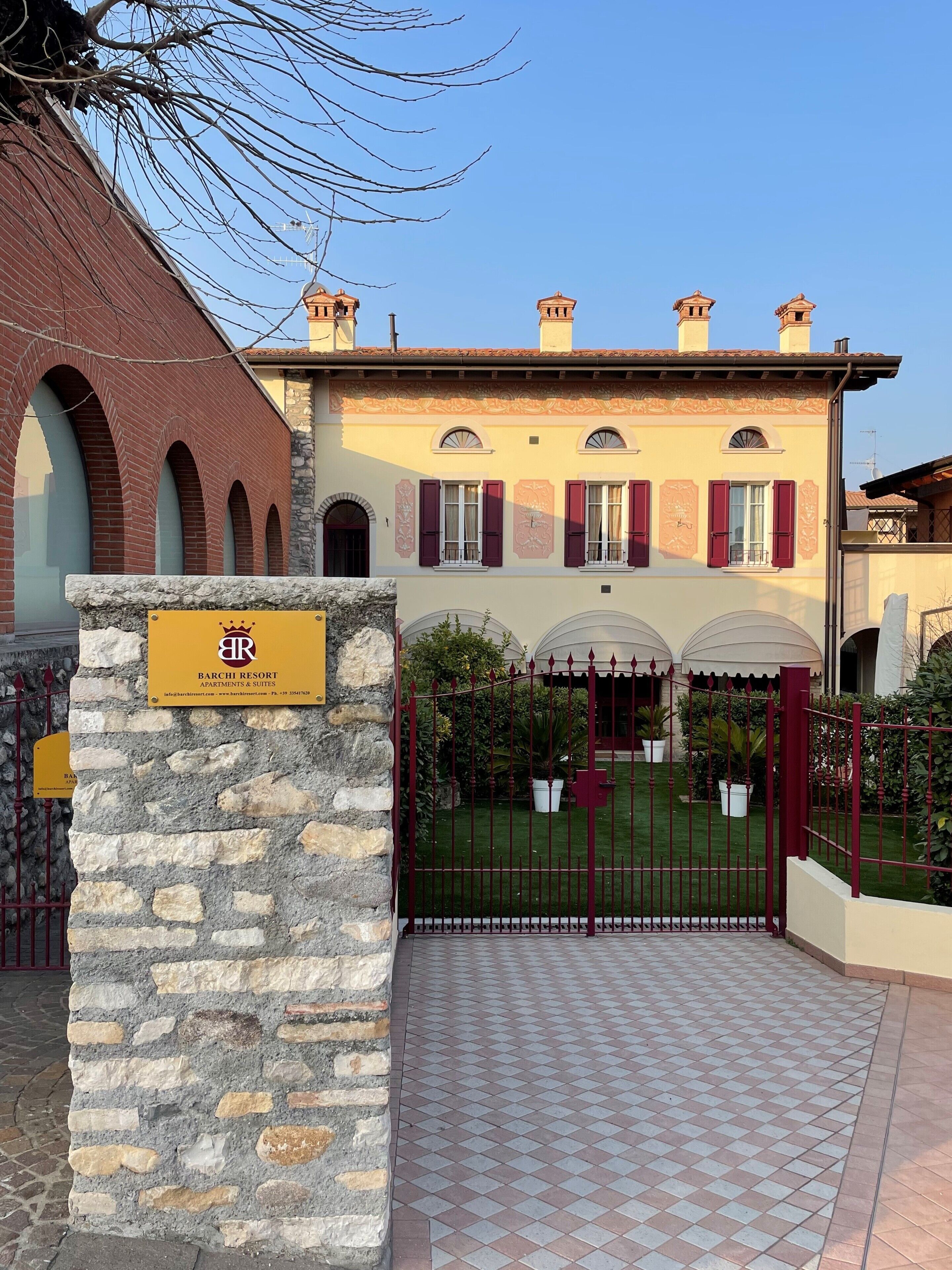 A stone entrance gate with a sign for Barchi Resort, featuring a brick building with arched windows and a manicured lawn.