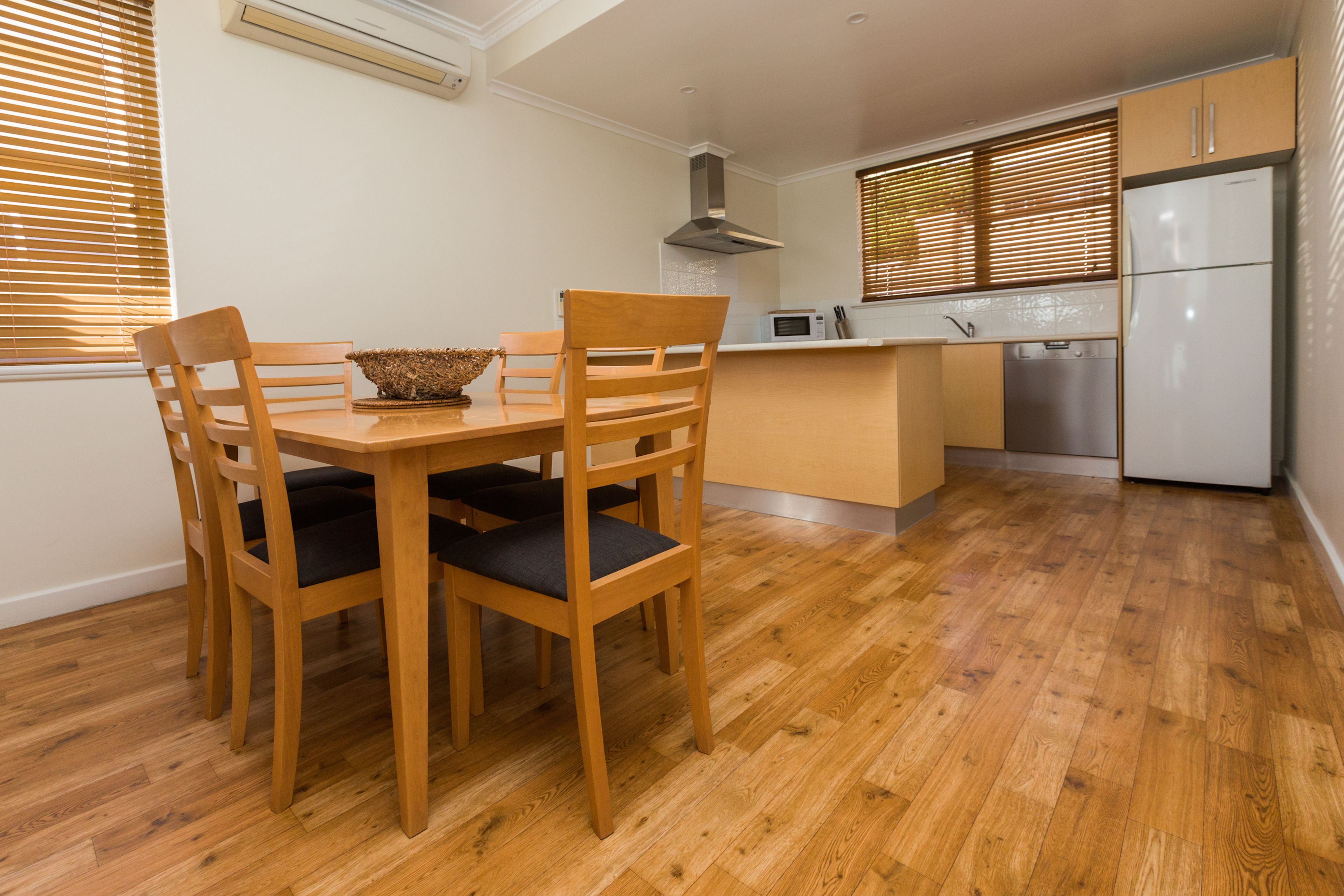 A compact kitchen with wooden flooring, a dining table with chairs, a microwave, a dishwasher, and a refrigerator.