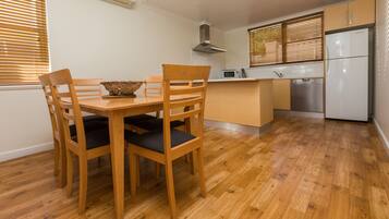 Una cocina compacta con piso de madera, una mesa de comedor con sillas, microondas, lavavajillas y refrigerador.