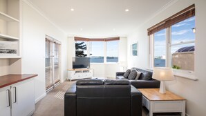 A modern living room with a sectional sofa, a TV, and a view of the water. - Bay 10 Accommodation (Port Lincoln)