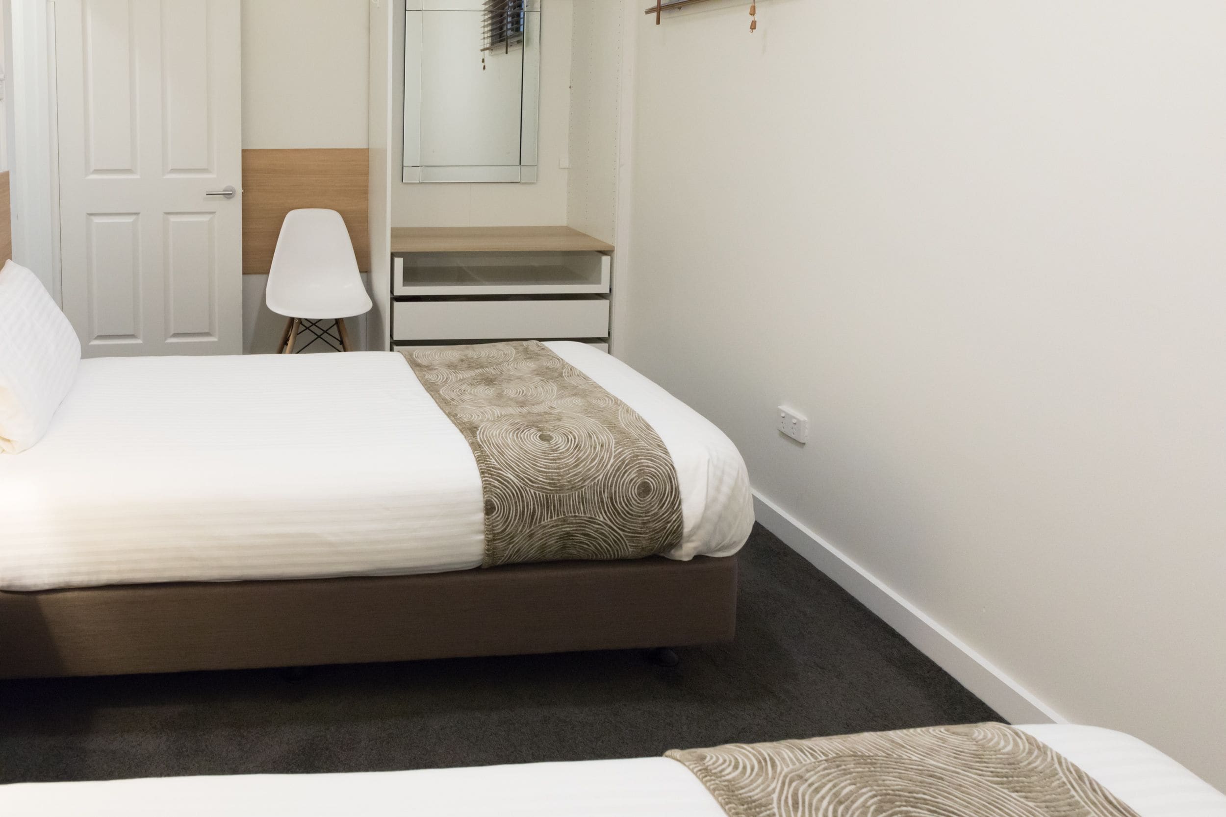 A bedroom with a bed, a chair, a desk, and a mirror.