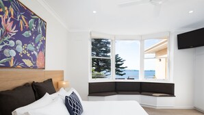 A bedroom with a large bed, a bay window with a view, a ceiling fan, and a mounted TV. - Bay 10 Accommodation (Port Lincoln)