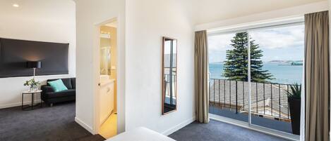 Habitación de hotel moderna con un balcón grande, un televisor de pantalla plana y vista al mar.