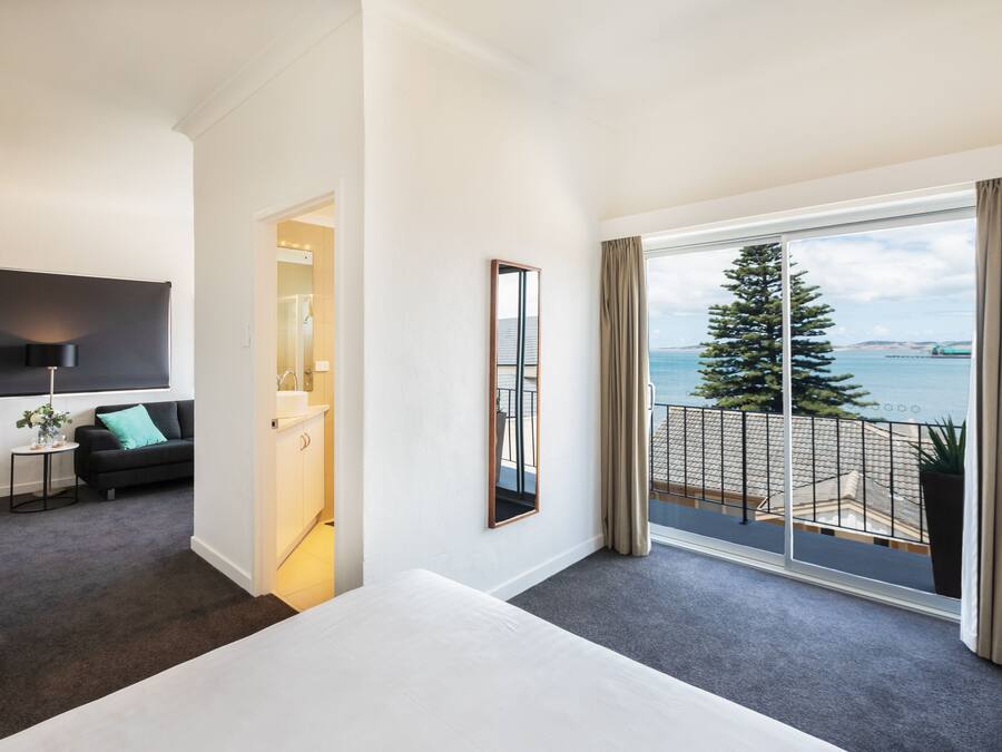 A modern hotel room with a large balcony, a flat-screen TV, and a view of the sea.