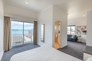 Ett hotellrum med en stor säng, en balkong med utsikt över havet, en soffa och ett litet bord med en växt.