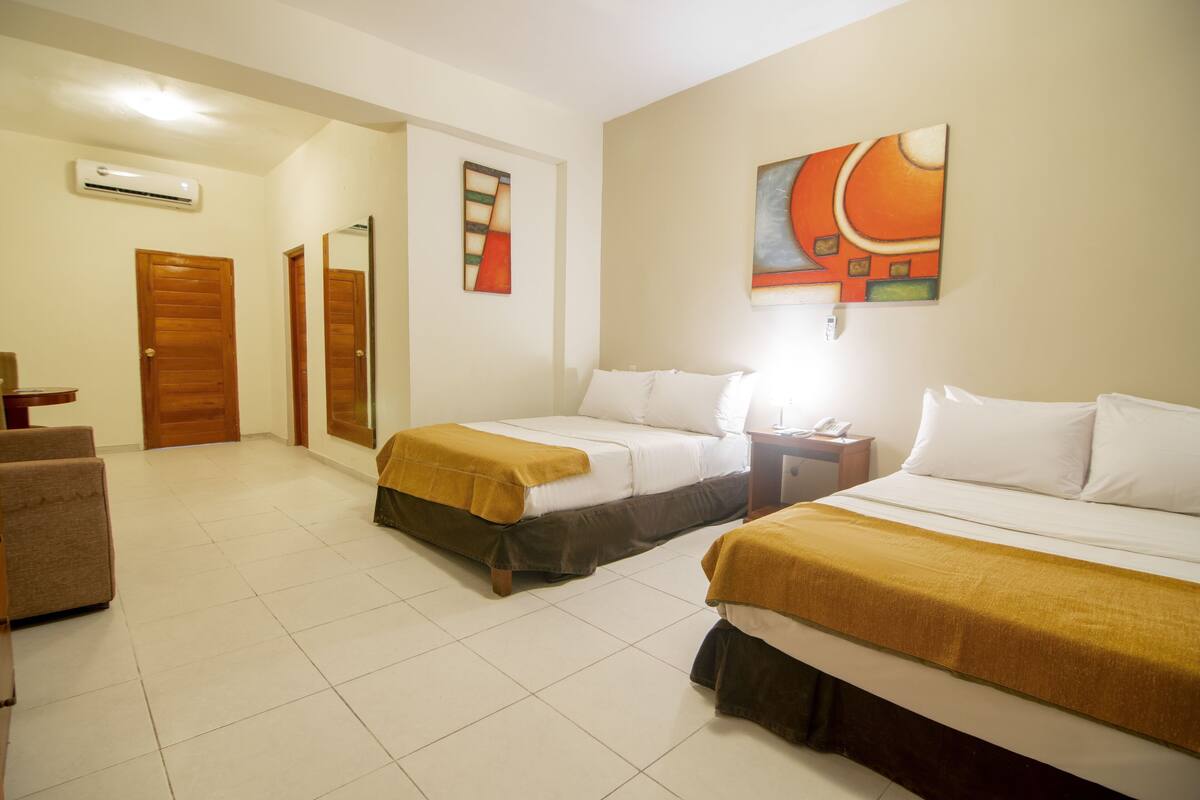 Habitación de hotel con dos camas, una puerta de madera, un espejo y un cuadro en la pared.