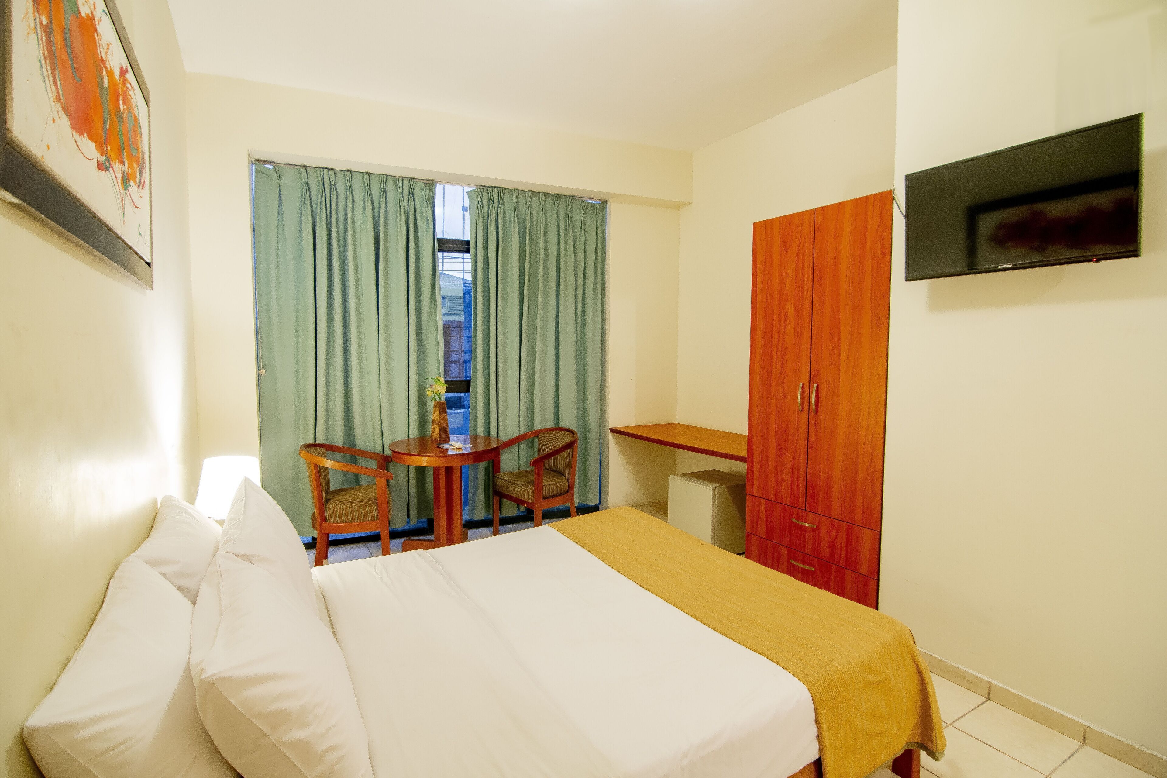 A hotel room with a bed, a desk, a chair, a television, and a wardrobe.