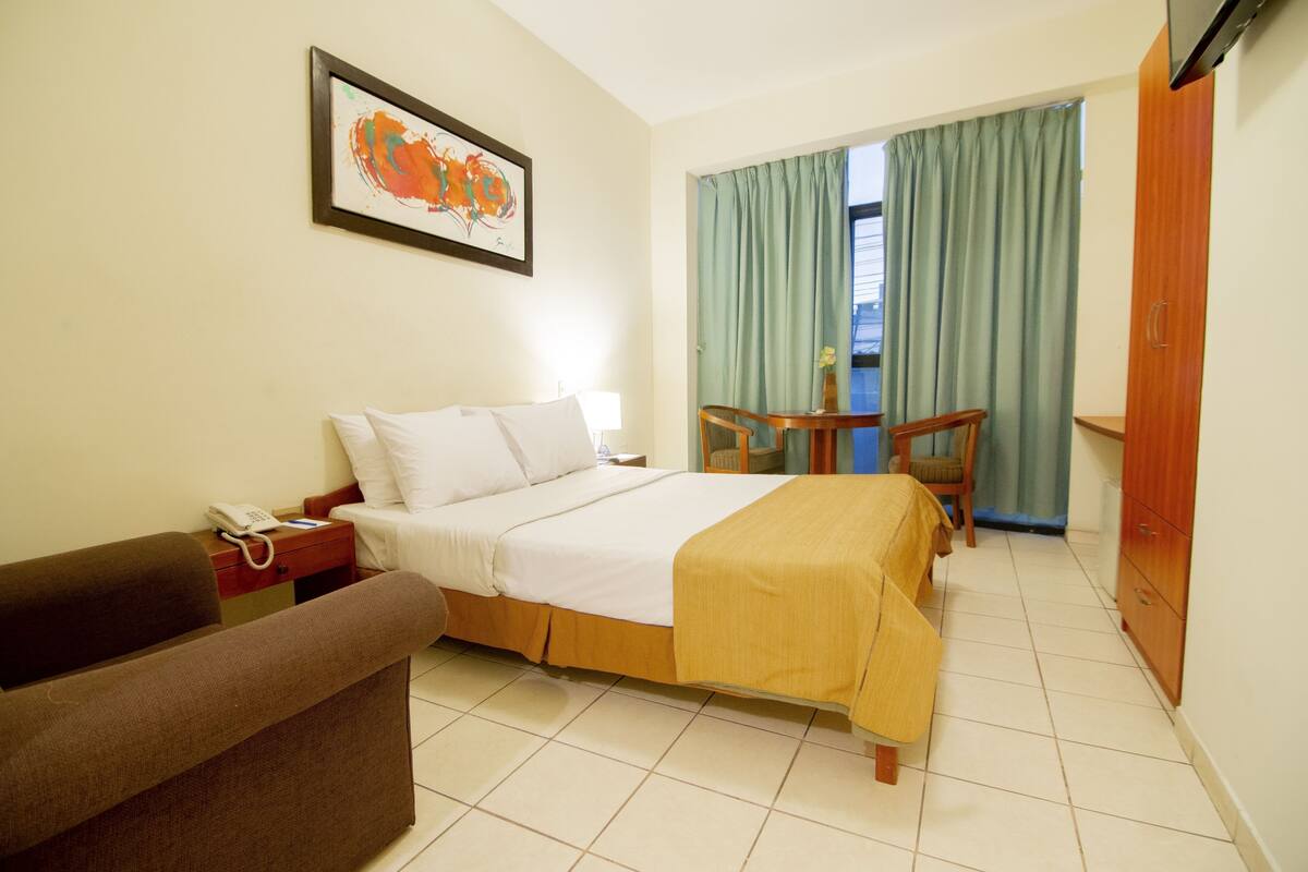 Habitación de hotel con cama, una silla, una mesita, un sofá y un cuadro en la pared.