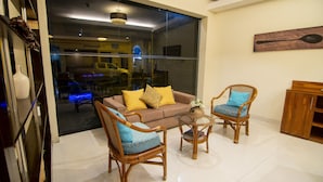 A modern living room with a brown sofa, two wicker chairs, a glass coffee table, and a wooden cabinet.