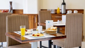 A breakfast table with a plate of food, a glass of orange juice, a basket of bread, and a coffee maker.