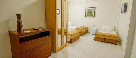 Una habitación de hotel con un aparador de madera, dos camas individuales con cubrecamas amarillos, una mesita de noche con lámpara y un cuadro enmarcado en la pared.