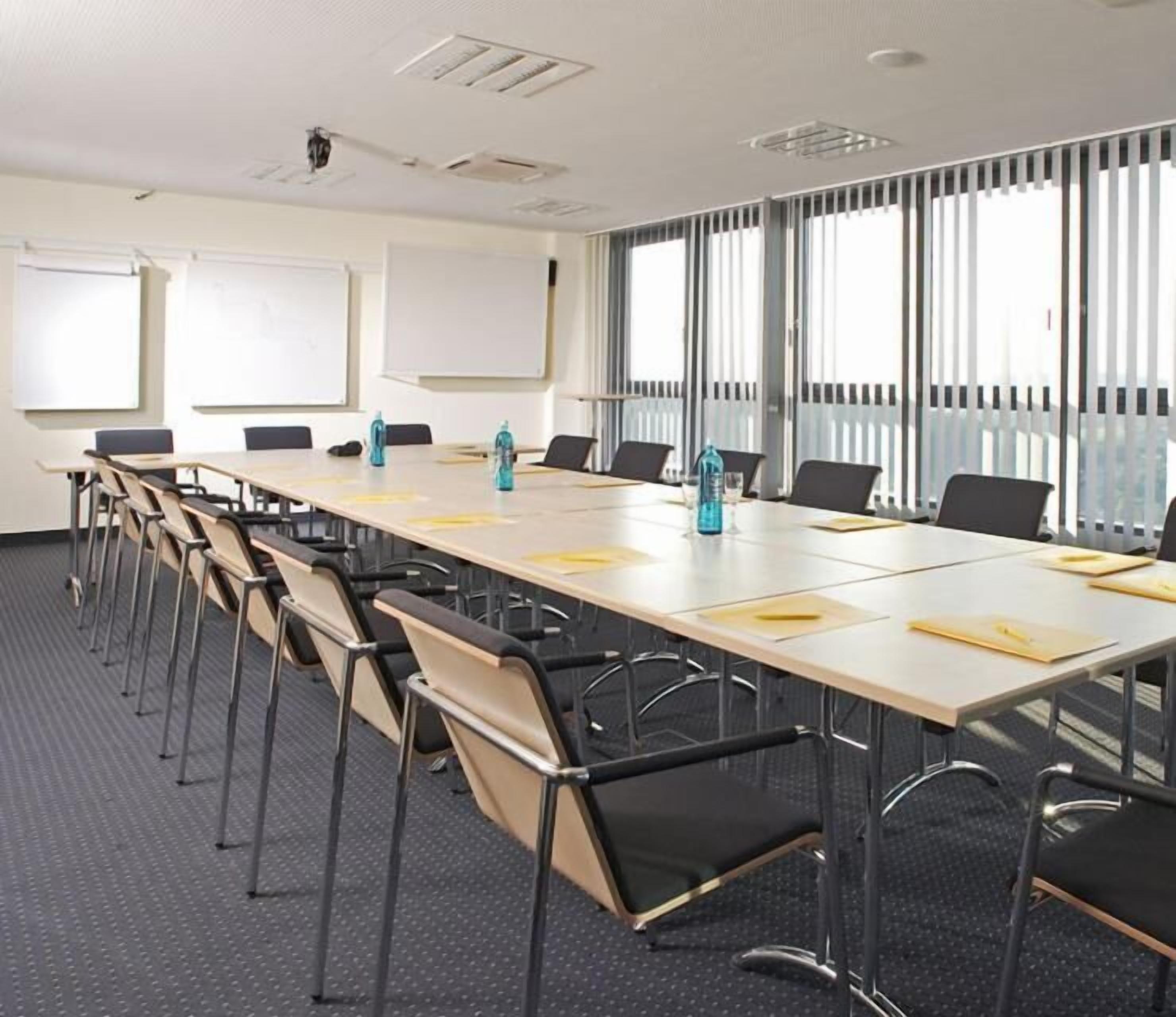 A conference room with a long table, chairs, a whiteboard, and large windows with blinds.