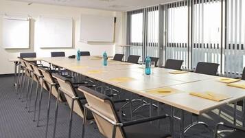 Un salón de conferencias con una larga mesa, sillas, una pizarra y ventanas amplias con persianas.