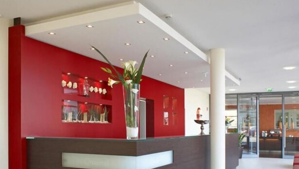 A reception area with a red and brown counter, a vase with flowers, and a glass door leading to another room.