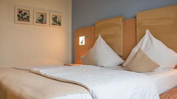 Un lit bien fait, avec une literie blanche et des oreillers beige, une tête de lit en bois et trois tableaux encadrés représentant des motifs floraux accrochés au mur.