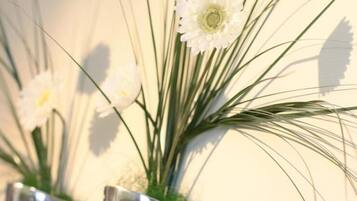 A close-up of white flowers in a metallic vase against a plain wall.