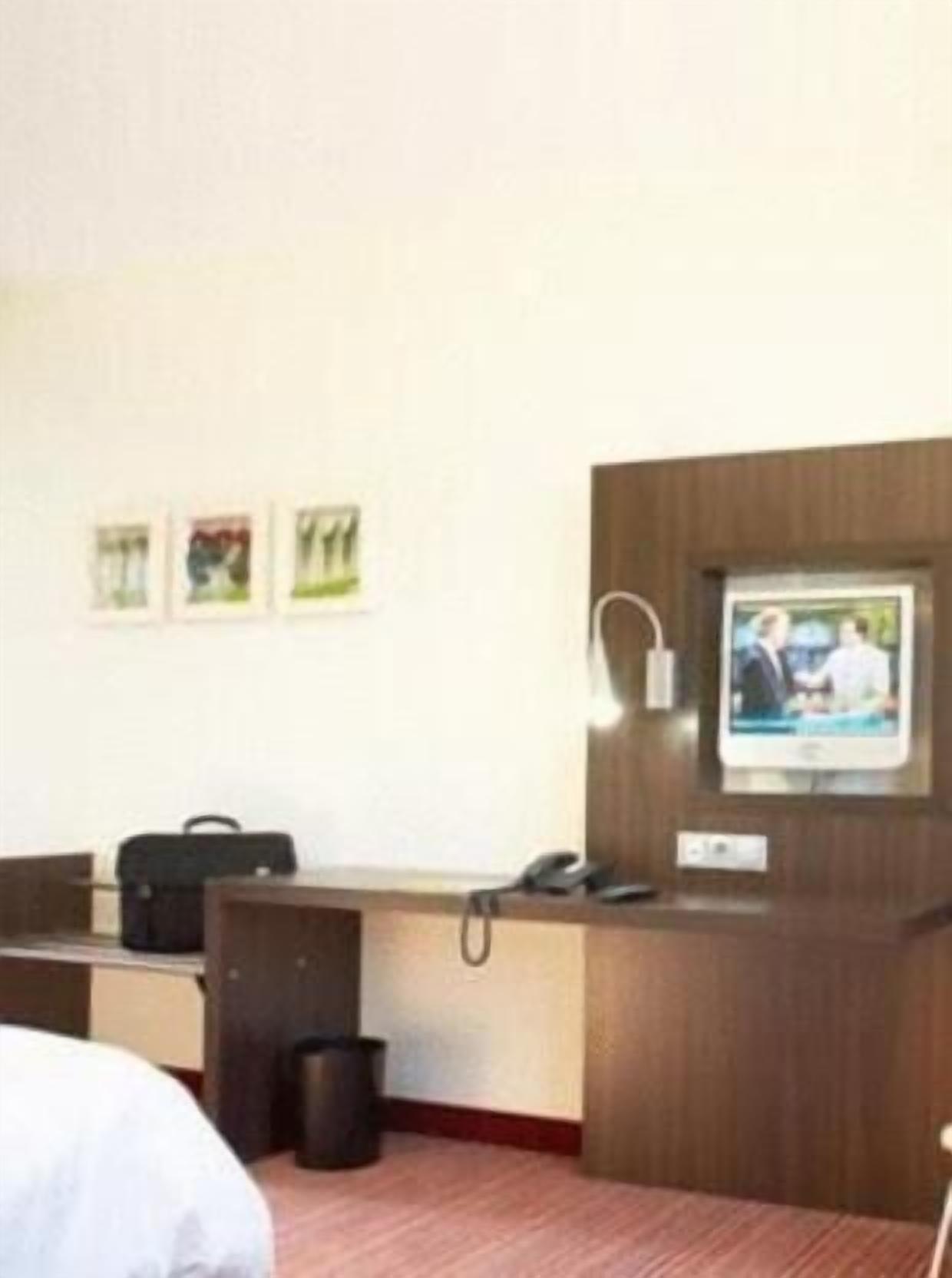 Habitación de hotel con cama, escritorio, cubo de basura y televisor instalado en la pared.