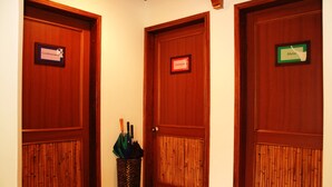 Three wooden doors with nameplates, a bamboo-patterned door panel, and a trash bin with umbrellas. - Zuetana 106 (Bogotá)