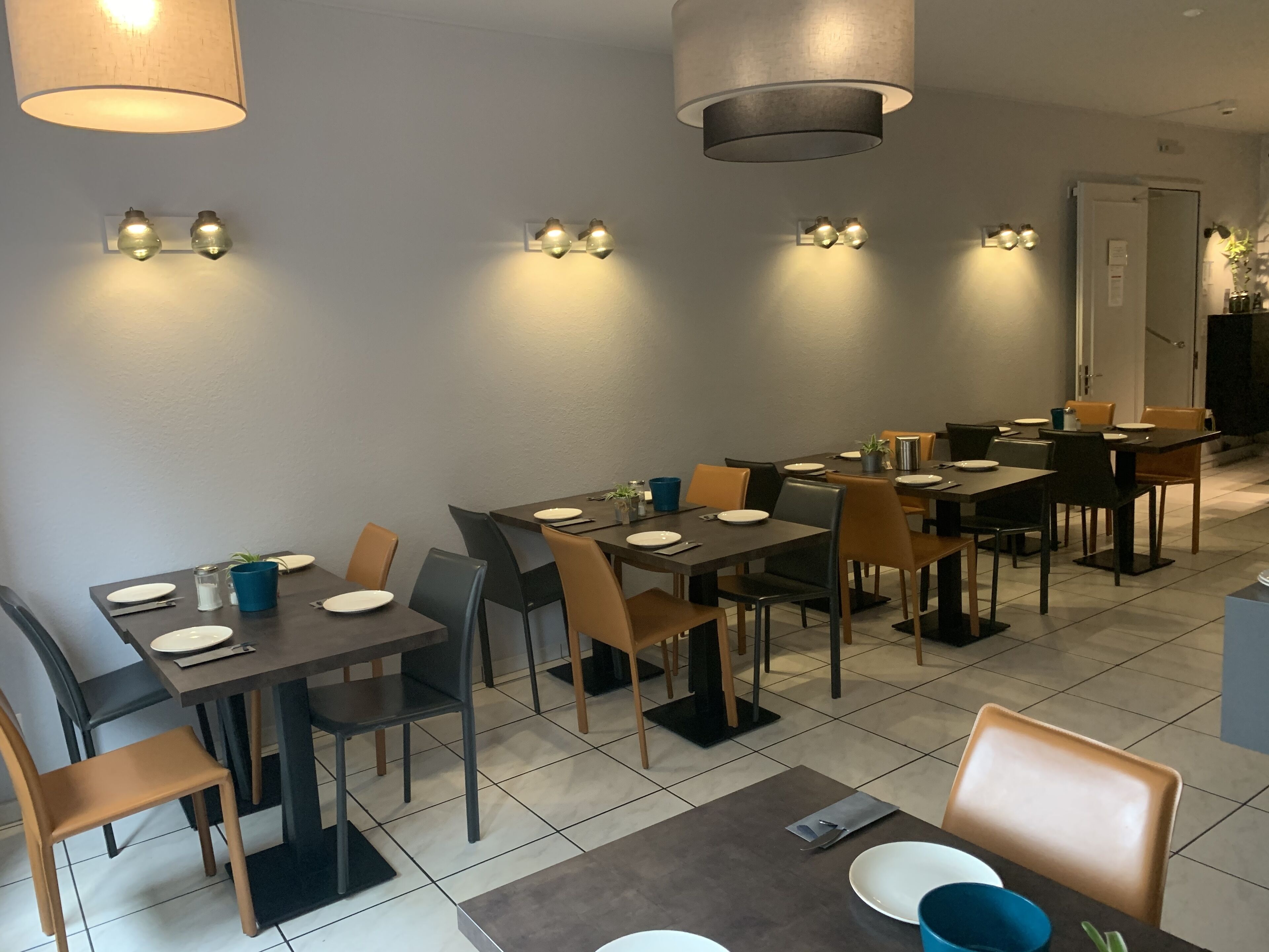 Un espace repas comprenant plusieurs tables et chaises, un éclairage d’ambiance et un sol carrelé.