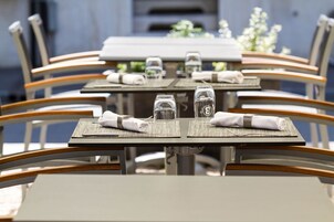 Un comedor con mesas dispuestas para cuatro, cada una con un mantel individual, servilleta doblada y un vaso de agua.