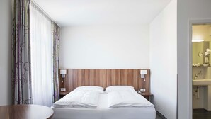 Ein Hotelzimmer mit Bett, Nachttischen, einem kleinen Holztisch und Blick ins Bad.