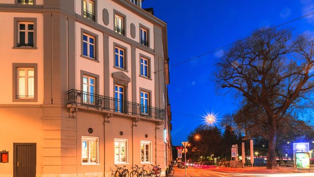 Ein mehrstöckiges Gebäude mit einer Fensterreihe im Erdgeschoss, einem Balkon im zweiten Stock und Fahrrädern davor.