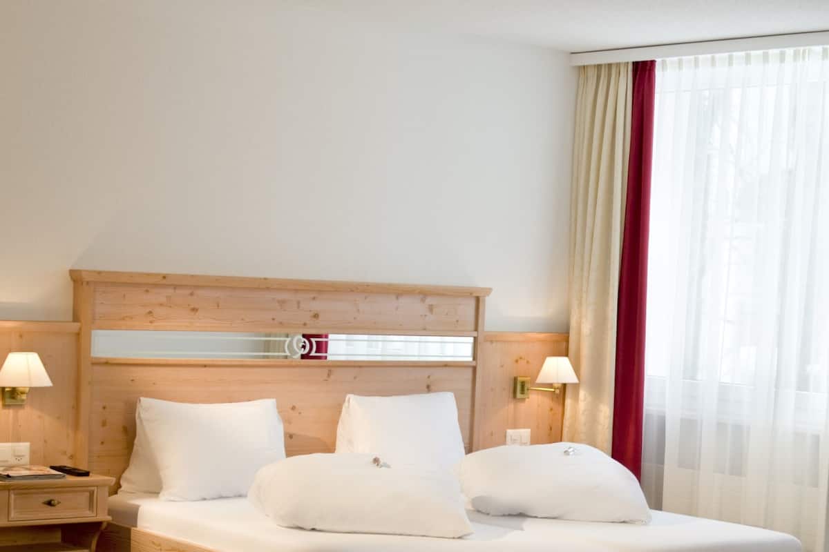 A neatly made bed with a wooden headboard, two bedside tables with lamps, and a window with sheer curtains.