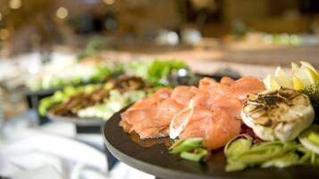 Un bufé con distintos alimentos, incluyendo salmón, verduras y preparaciones a la parrilla.