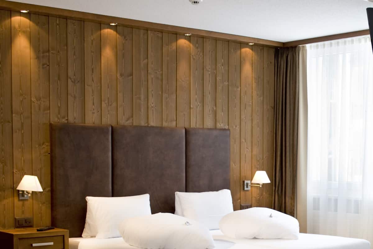 A double bed with a wooden headboard, two bedside tables with lamps, and a large window with curtains.