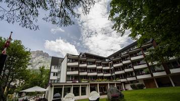 A multi-story hotel with balconies, outdoor seating, and a mountain backdrop.