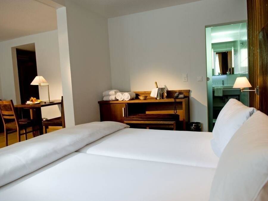 A hotel room with a bed, a desk with a lamp, a chair, and a small table with toiletries.