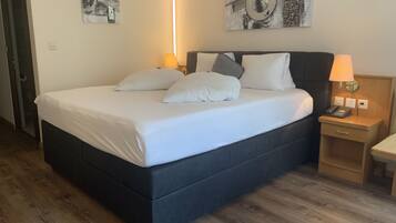 A neatly made bed with white linens and pillows, a bedside table with a lamp, and artwork on the walls.