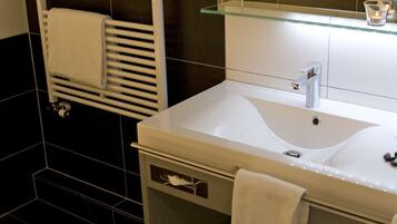 A modern bathroom with a white sink, a glass shelf above it, and a towel rack with towels.