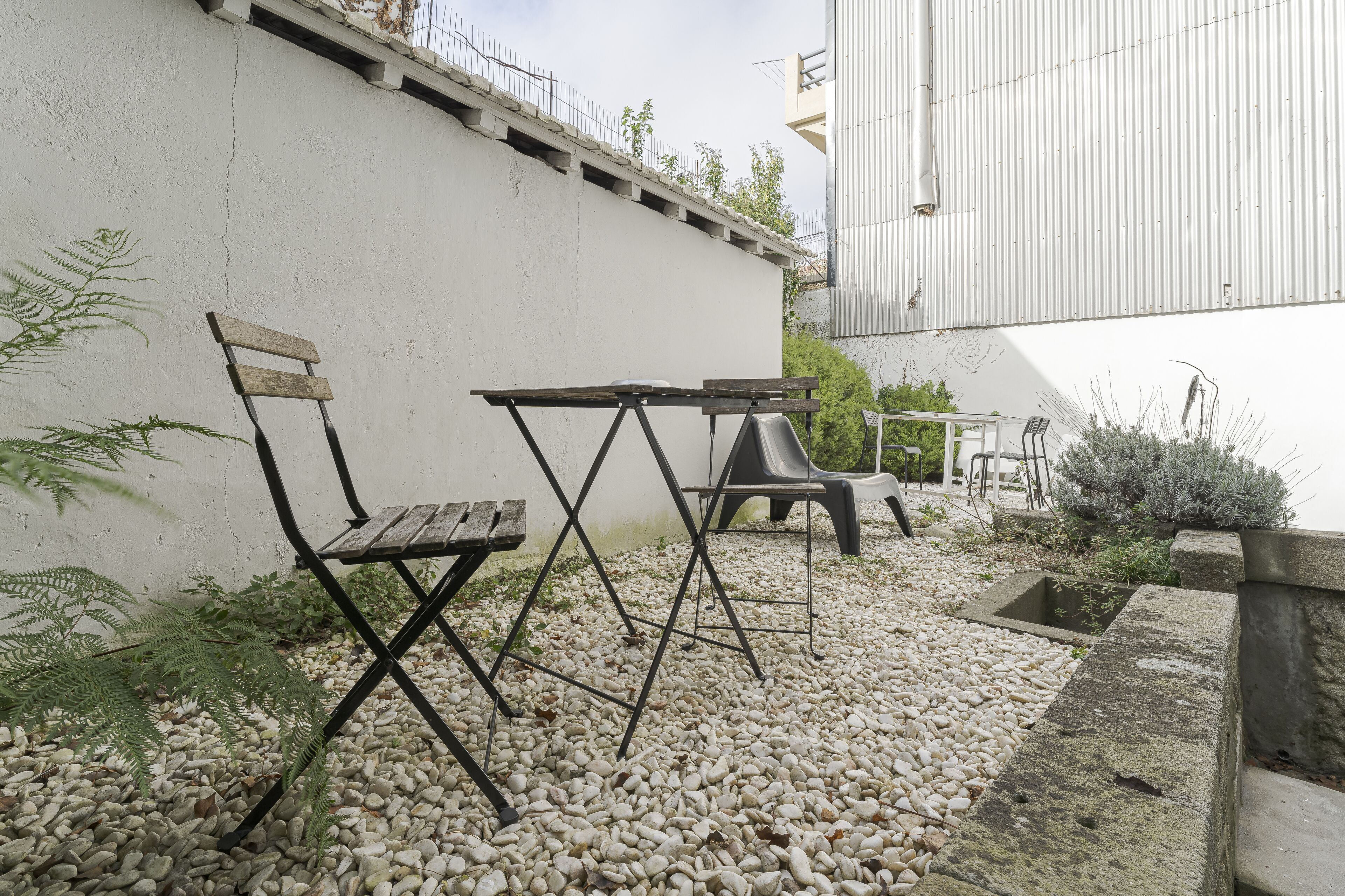 An outdoor seating area with a white wall, a metal fence, and a gravel ground.