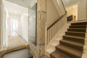 Una escalera con peldaños alfombrados y barandilla, que conduce a una habitación con una puerta blanca y una ventana.