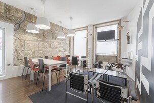Una sala de conferencias moderna con pared de piedra, mesas blancas y sillas negras y rojas.