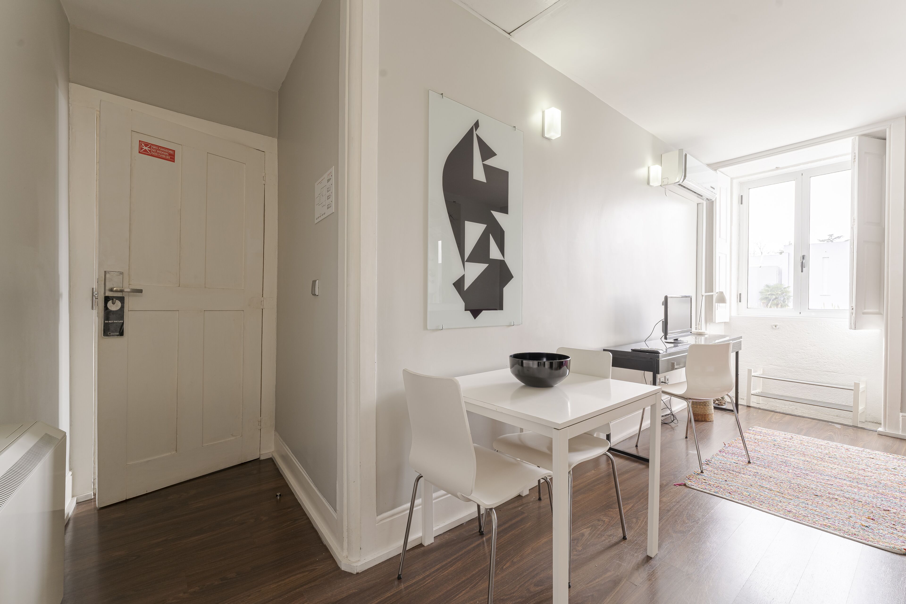 A modern dining area with a white table and chairs, a black bowl, and a geometric wall art piece.