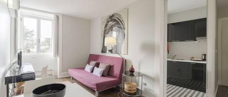 Una sala de estar moderna con un sofá rosa, una mesa blanca y una zona de cocina con armarios y encimera.